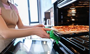 En kvinne setter en pizza i ovnen