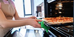 En kvinne setter en pizza i ovnen
