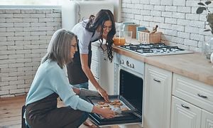 To kvinner på et kjøkken som putter stekeplate med kjeks inn i ovnen