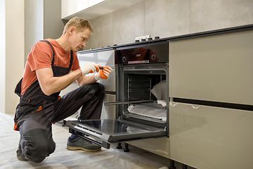 Tekniker reparerer en stekeovn på et kjøkken