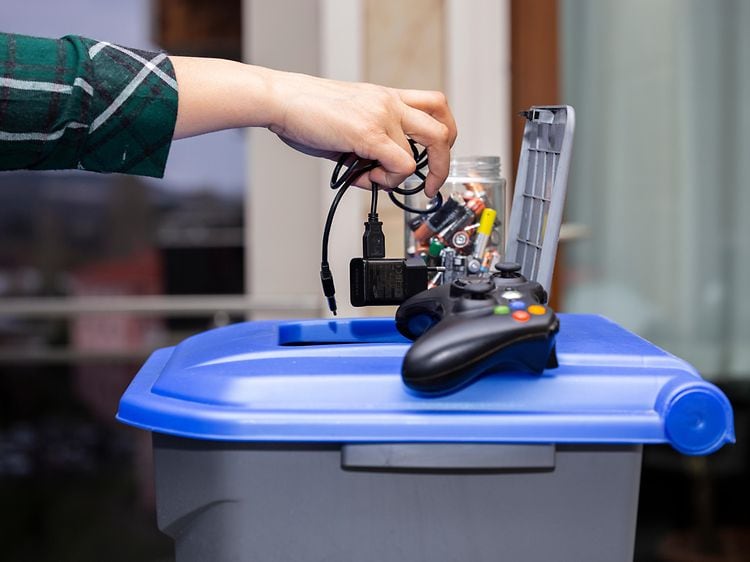 En hånd som kaster gammel elektronikk i søppelbøtte
