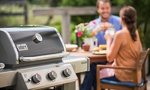 Weber gassgrill og et par som spiser middag utendørs i bakgrunnen