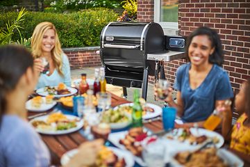 personer spiser middag ute med en svart Weber pelletsgrill i bakgrunnen