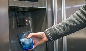 En person fyller isbiter i et vannglass fra kjøleskapet