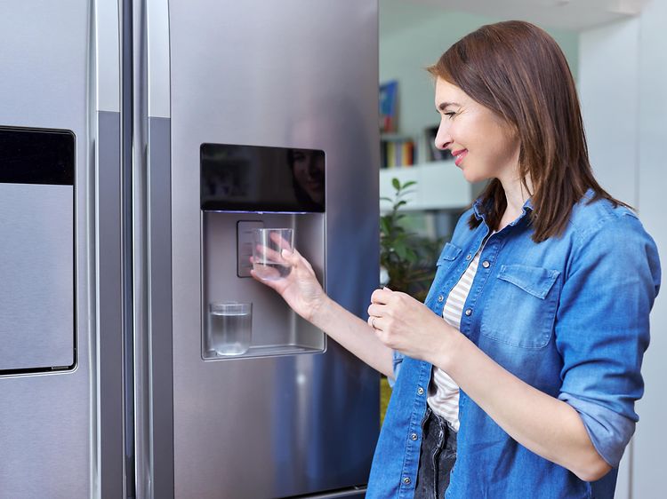 En kvinne henter is i vannglasset fra kjøleskapet