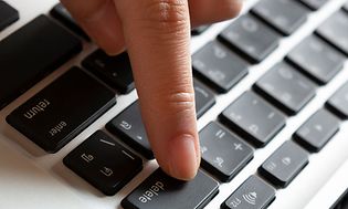 Hånd som trykker på delete-knappen på et tastatur