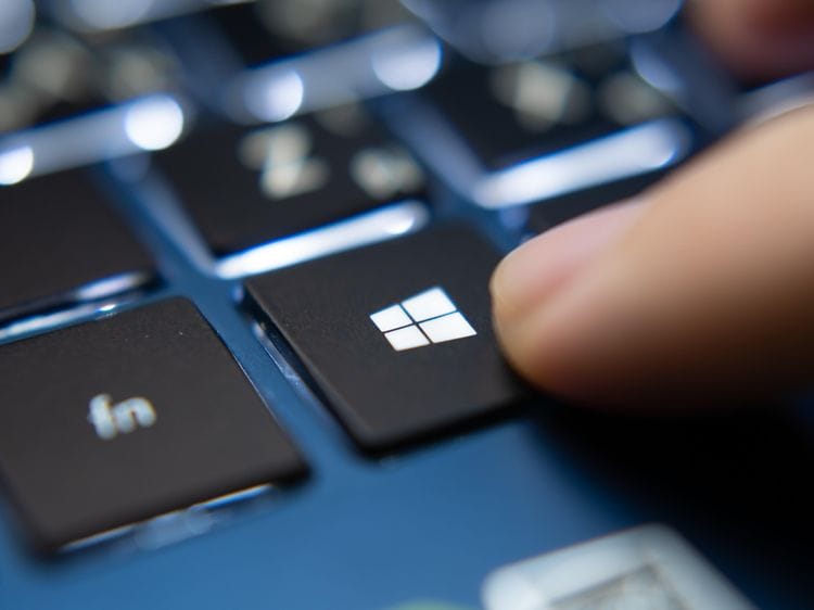 Finger som trykker på Microsoft Windows-tast på blå bærbar PC