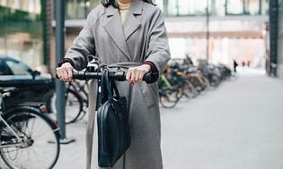 En kvinne kjører el-sparkesykkel med en veske på styret