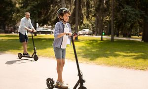 En ung gutt kjører el-sparkesykkel sammen med faren sin i en park