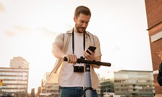 En mann med kamera rundt halsen sjekker mobilen på en el-sparkesykkel