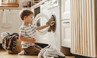 En liten gutt laster klær og bamser inn i vaskemaskinen
