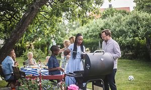 Mange mennesker samlet rundt en grill i en grønn hage