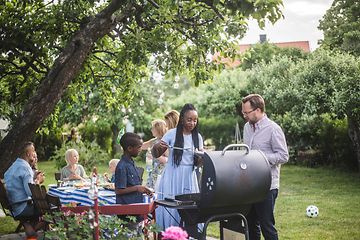 Mange mennesker samlet rundt en grill i en grønn hage