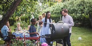 Mange mennesker samlet rundt en grill i en grønn hage