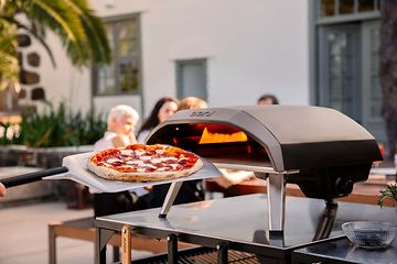 en pizza foran en pizzaovn og mennesker i bakgrunnen