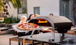 en pizza foran en pizzaovn og mennesker i bakgrunnen