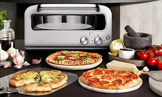 Ulike typer pizza på et bord og en pizzaovn fra Sage i bakgrunnen