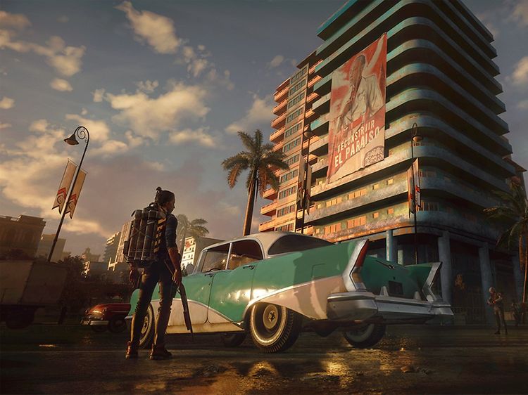 Far Cry 6 - Kvinne med flammekaster i hånden som står foran en bil foran en høy bygning