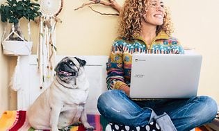 Kvinne jobber på en Acer Chromebook med en hund ved siden av seg