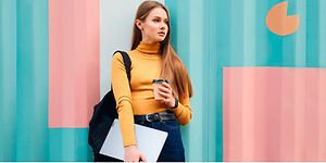 kvinne foran en flerfalget vegg med en Lenovo IdeaPad 5 og en kaffekopp i hendene