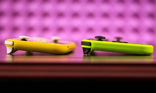 en gul og en grønn Nintendo Switch Lite liggende mot lilla bakgrunn