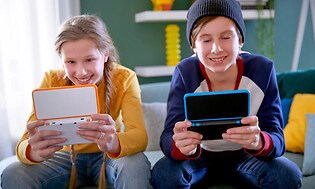 gutt og jente spiller på hver sin Nintendo 2DS XL