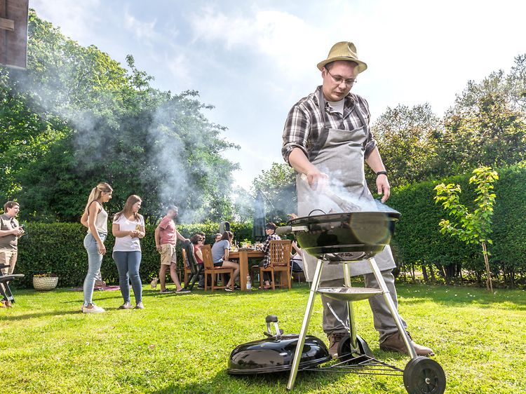 en mann griller i hagen og mennesker står og sitter bak ham