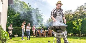 en mann griller i hagen og mennesker står og sitter bak ham