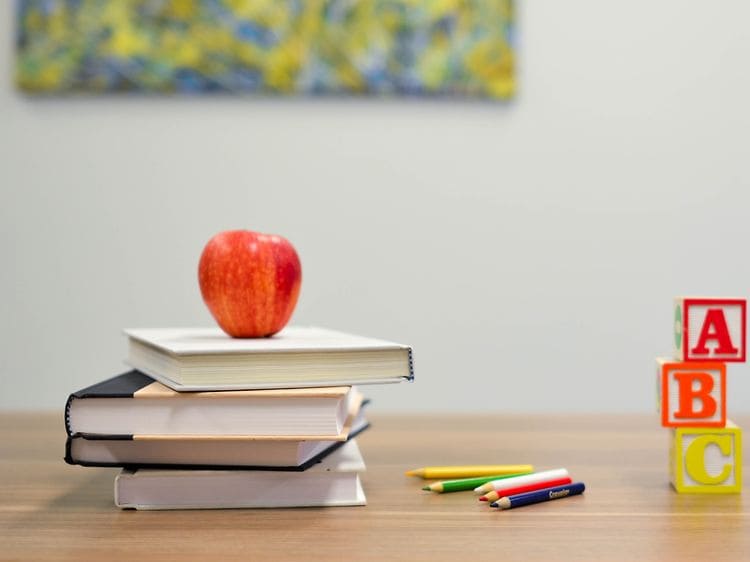 Bøker, fargeblyanter og et eple på et bord