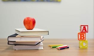 Bøker, fargeblyanter og et eple på et bord