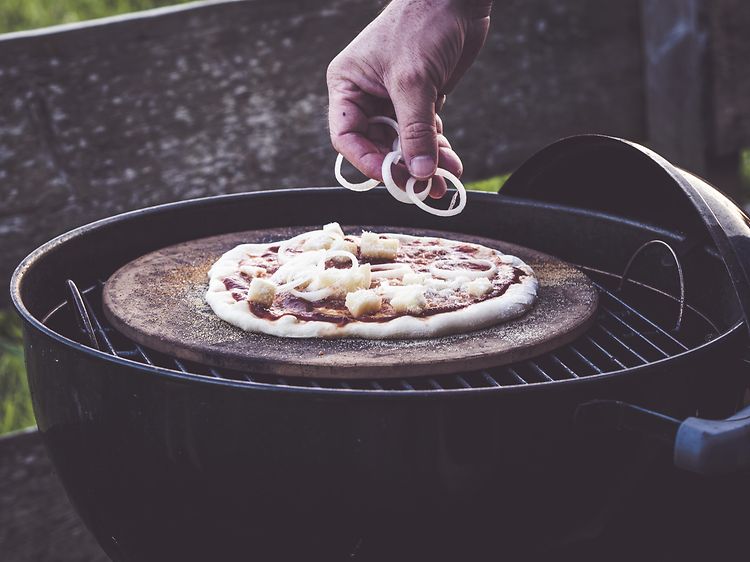 Person som putter topping på en pizza