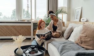 To kvinner i en sofa, leser en bok og en luftkvalitetsmonitor bak dem