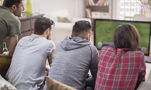 Fire menn sitter i en sofa og ser fotball på TV