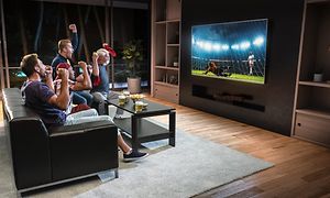 Folk ser fotball på en stor TV i en stue og heier