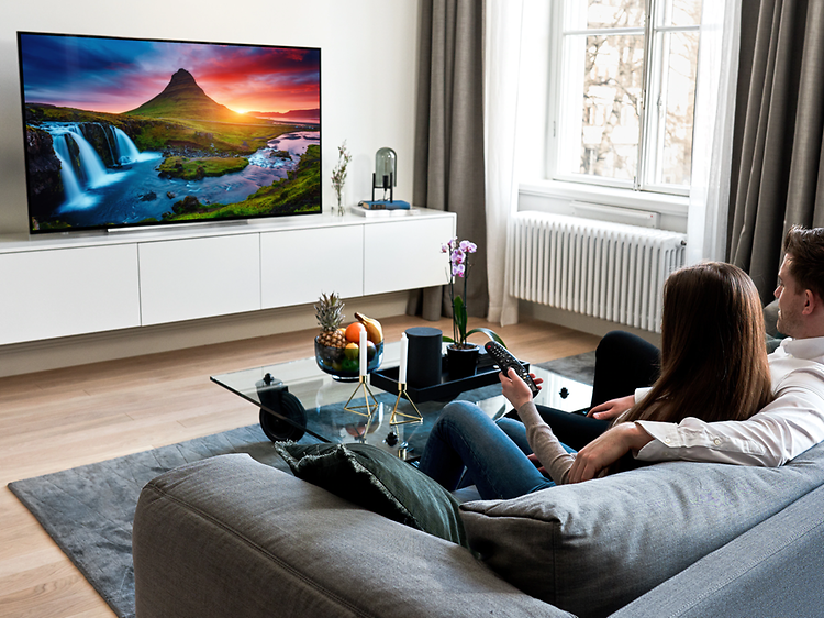 par sitter i sofa og ser på tv med fargerrikt landskapsbilde
