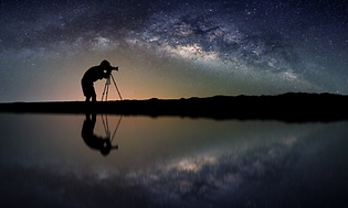 Stående mann med kamera på horisontkant med stjernehimmel i bakgrunnen