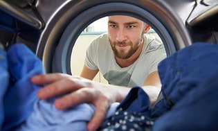 mann henter klær fra inne i vaskemaskin