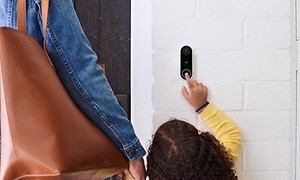 liten jente i gul genser ringer på smart dørklokke ved siden av en voksen