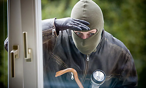 Maskert person med lommelykt ser inn gjennom vindu