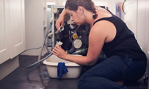 kvinne ser frustrert ut på gulvet mens hun ser på vannslangen til vaskemaskin