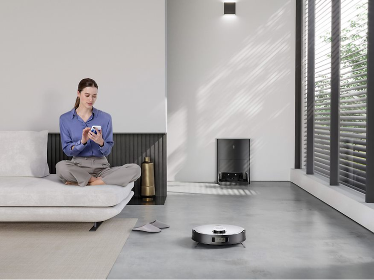 Ecovacs Deebot X1 på et gulv ved siden av en kvinne i en sofa