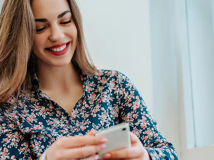 Kvinne smiler og ser ned på mobiltelefon