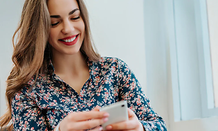 Kvinne smiler og ser ned på mobiltelefon