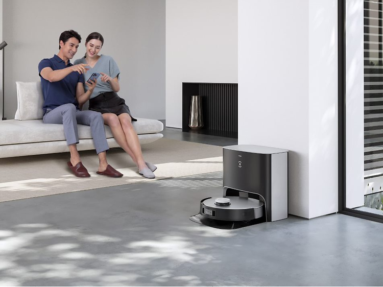 en Ecovacs Deebot X1 Plus lader, mens en mann og kvinne sitter i bakgrunnen