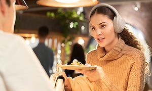 Kvinne med Sony hodetelefoner WH-1000XM4 på restaurant