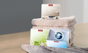 håndklær og bokser med vaskekapsler plassert på et bord