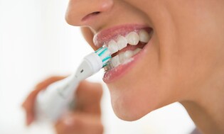 Kvinne pusser tennene med en elektrisk tannbørste