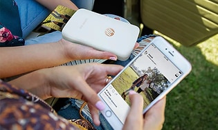 Personer som holder en HP Sprocket-skriver og smarttelefon med appen åpen