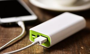 Powerbank som lader smarttelefon på kafébord ved siden av kaffekopp