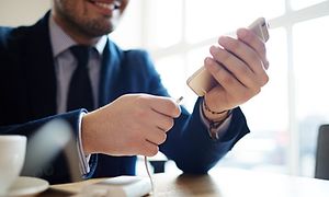 Smilende mann i dress som kobler powerbank til smarttelefon